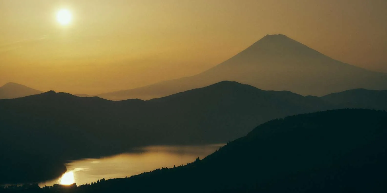 Mount Fuji silhouetted beyond layered hills