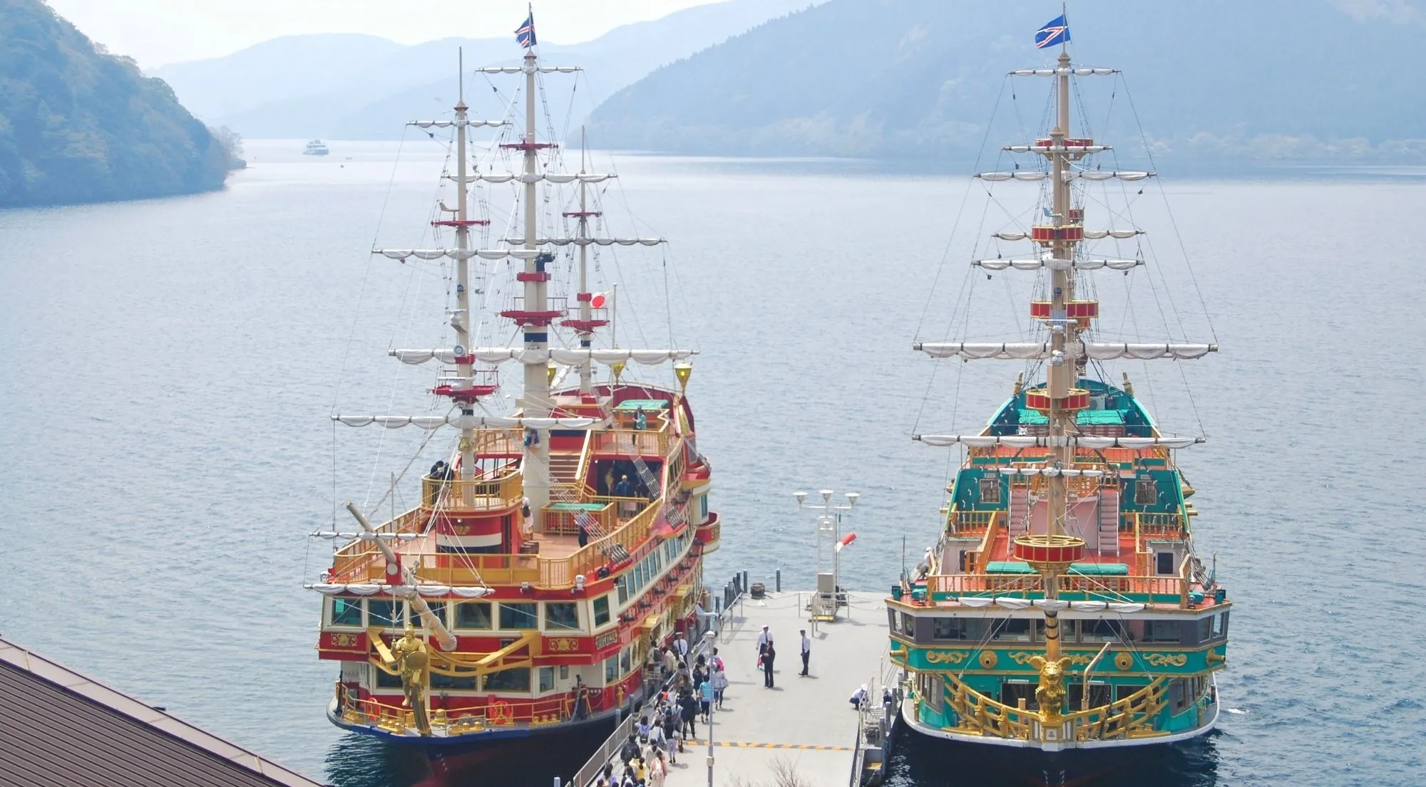 Two Hakone pirate ships moored at a Lake Ashi pier with mountains behind